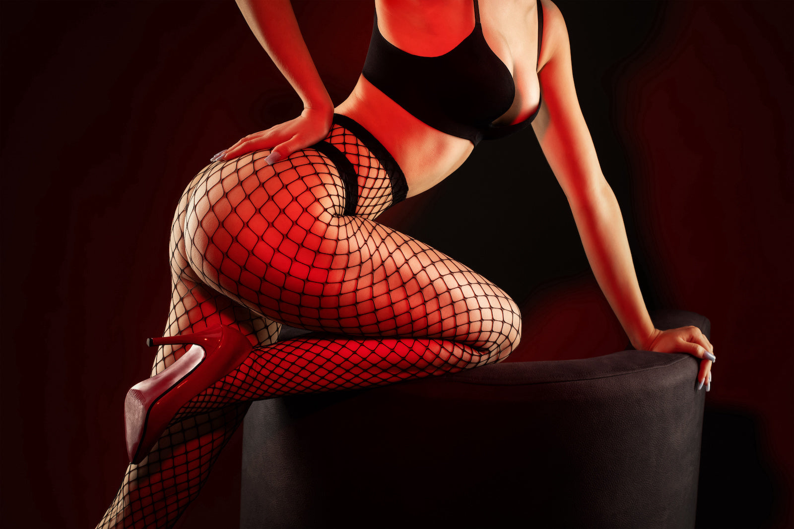 woman in fishnets tights and red heels leaning over a chair 